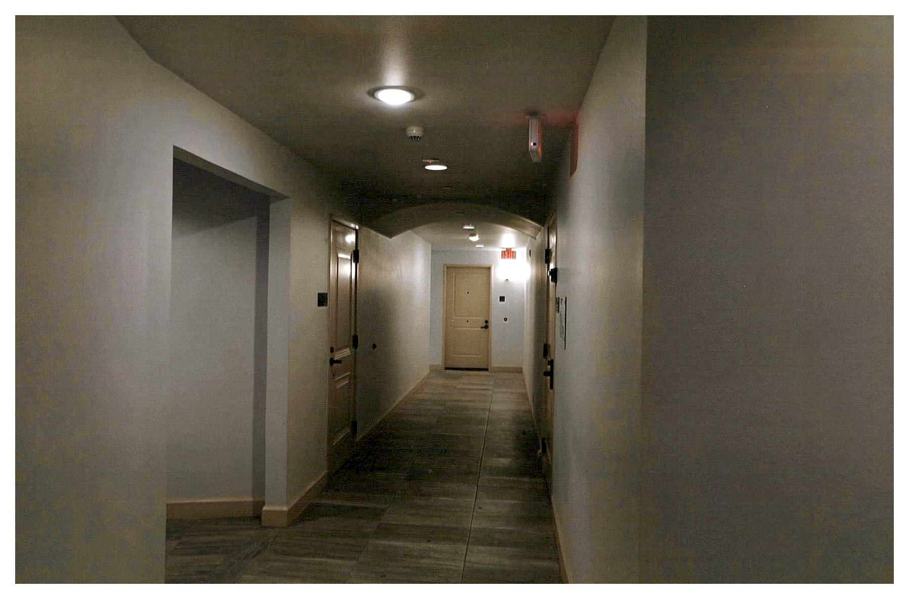 After:  view of refinished hallway with warm white walls, large tile floors and recessed ceiling fixtures in new hard shell dropped ceiling.