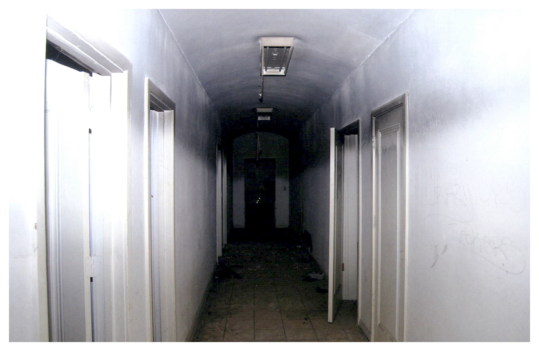 Before: same view of hallway with fluorescent utility lighting surface mounted to ceiling.