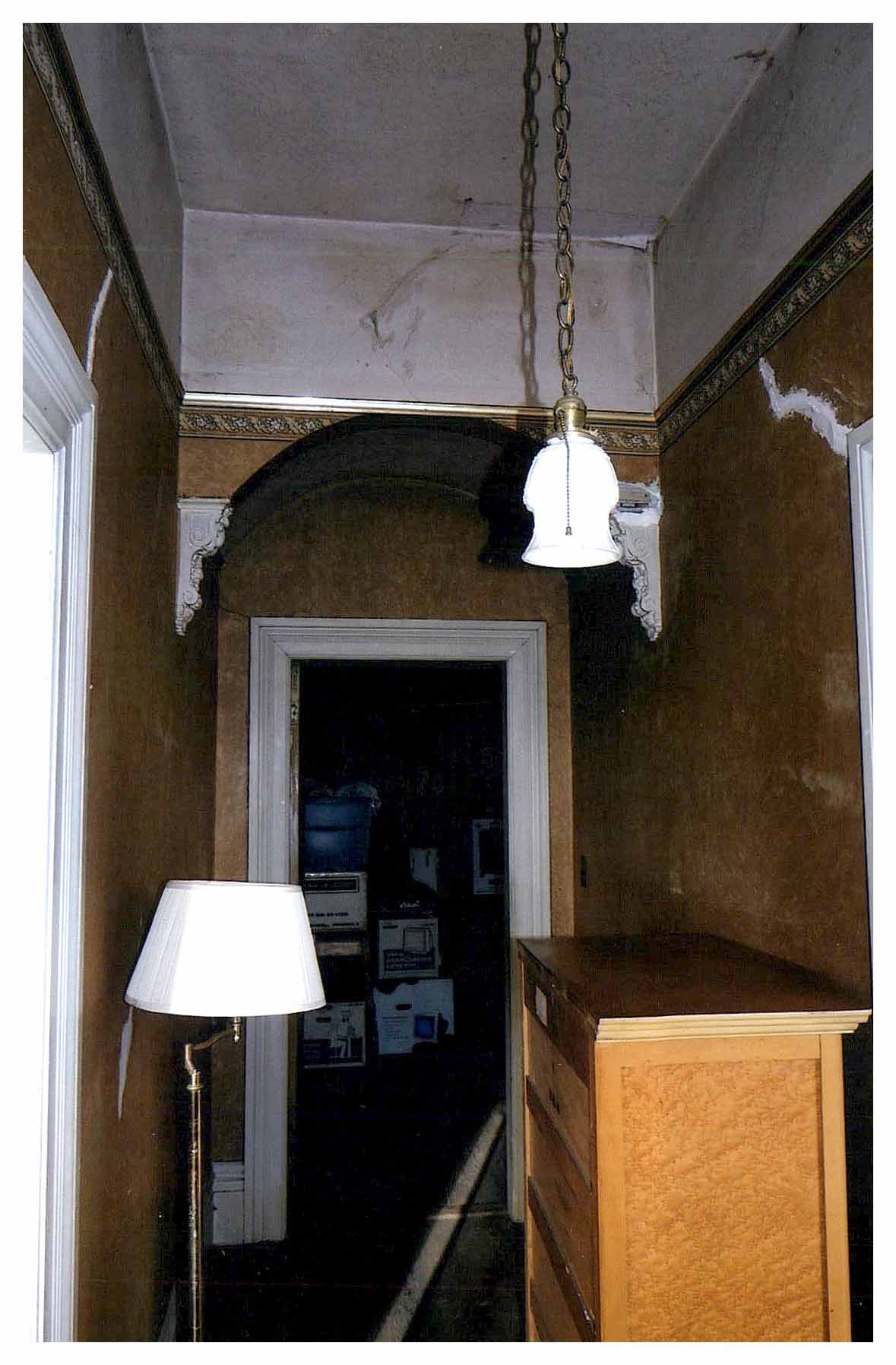 Before: view of end of hallway framing the unrepaired arch and broken ornamental brackets.