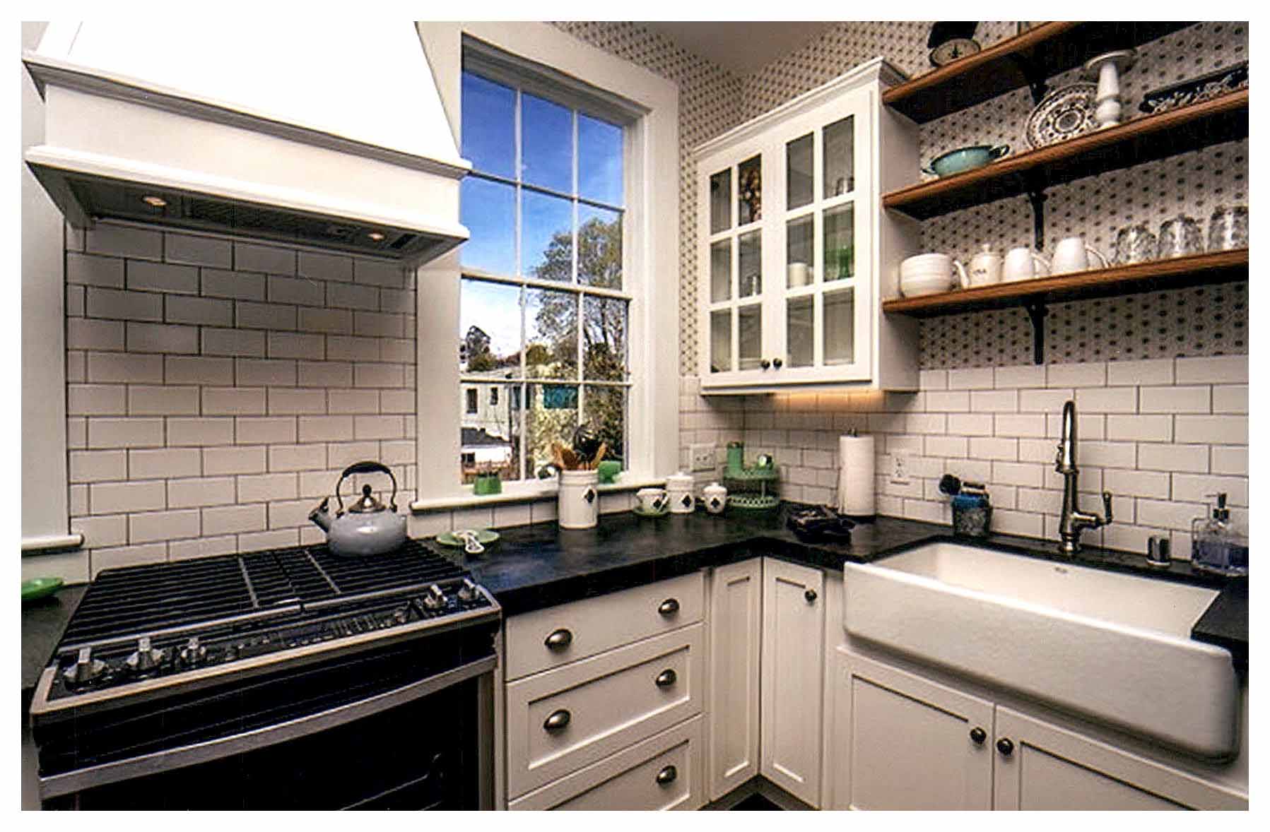 After: corner of new kitchen expanded into adjacent bathroom with window, wall cabinets, shelves, and white tile walls.