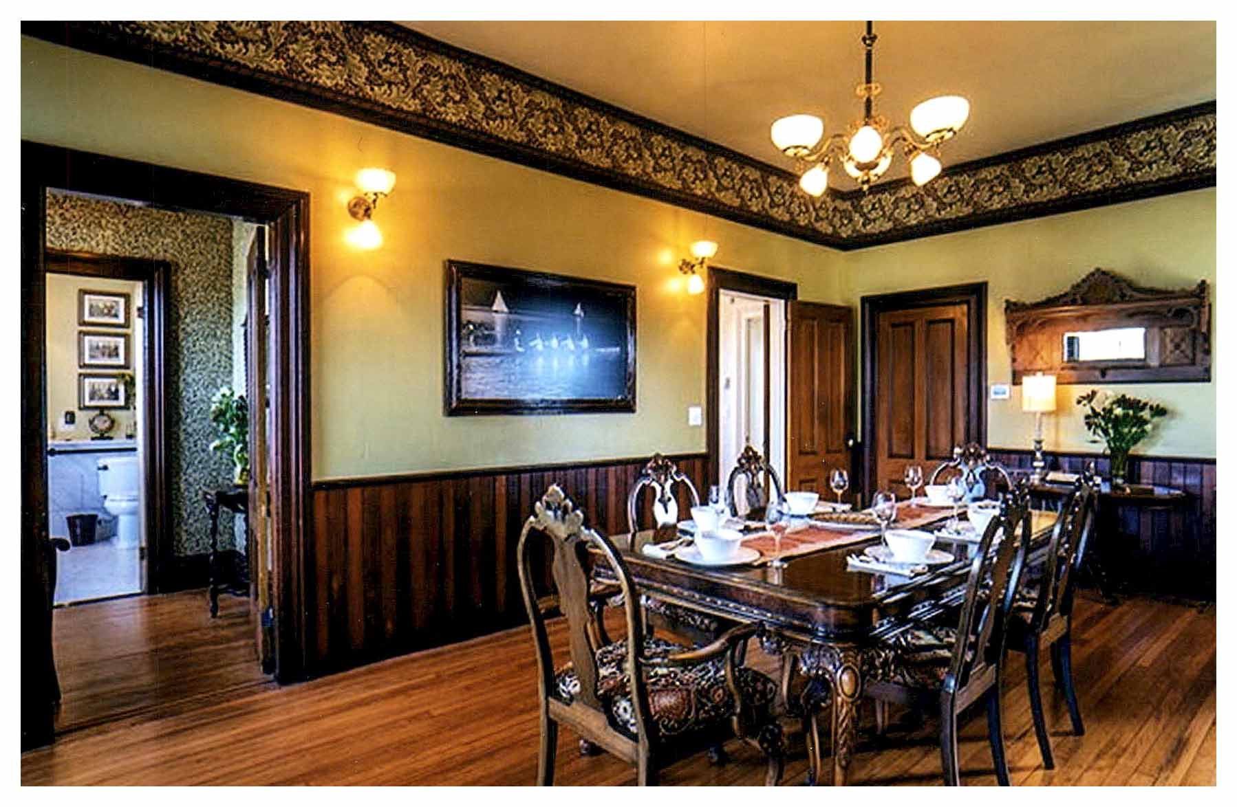 After: dining room with refinished wood floor and wainscot, wallpaper border at ceiling and new period light fixtures.