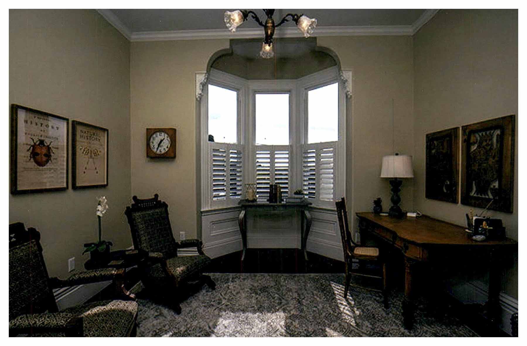 After: sitting room with a bay window in an arched-framed alcove and light beige painted walls.