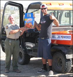 State Parks employee receiving large container of Crisco oil from a park visitor who is giving a thumbsup. Kubota UTV in the back ground.
