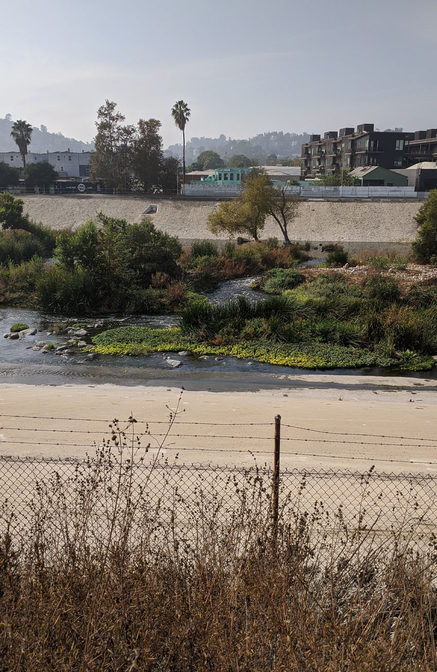 View of Los Angeles River showing water flowing and vegetation in the riverbed View of Los Angeles River showing water flowing and vegetation in the riverbed