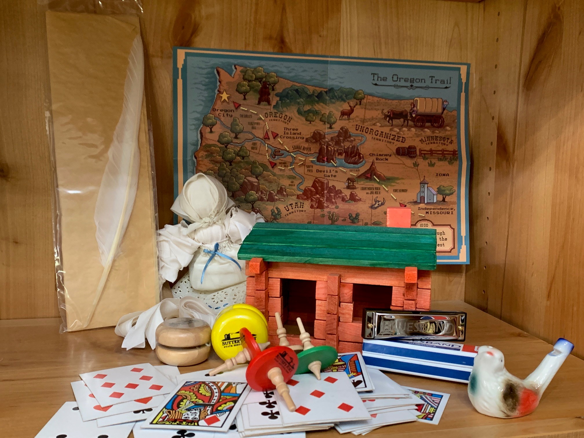 retail display shelf featuring various toys: quill, rag doll, playing cards, tops, harmonica, bird whistle, yo-yos, log cabin, Oregon Trail map retail display shelf featuring various toys: quill, rag doll, playing cards, tops, harmonica, bird whistle, yo-yos, log cabin, Oregon Trail map