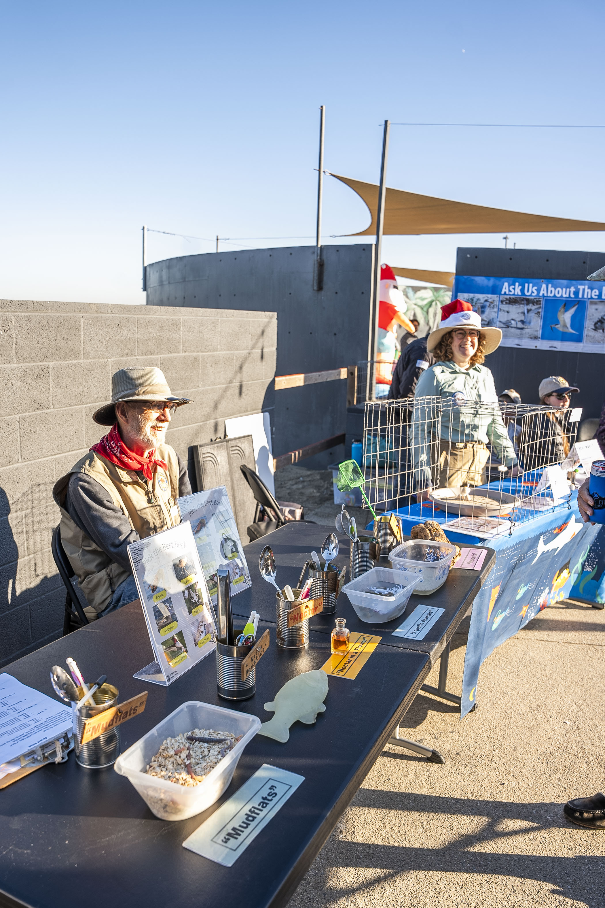 Two individuals stand at their booths with bird and scientific displays.